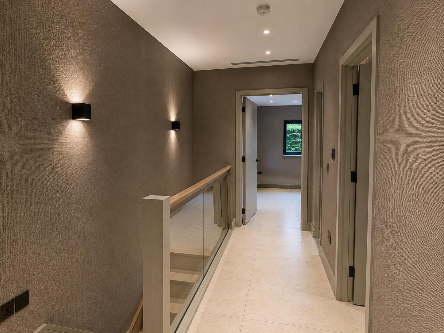Landing finished in a warm grey textured wallpaper with a glass balustrade