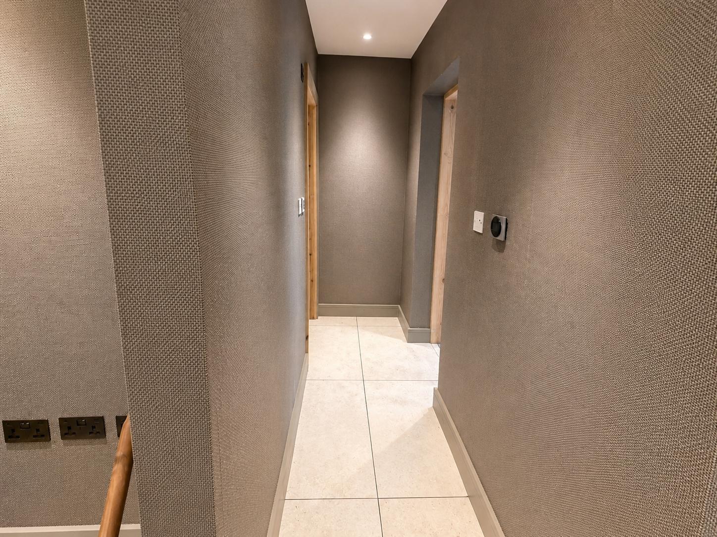 Narrow hallway papered in a textured grey wallcovering