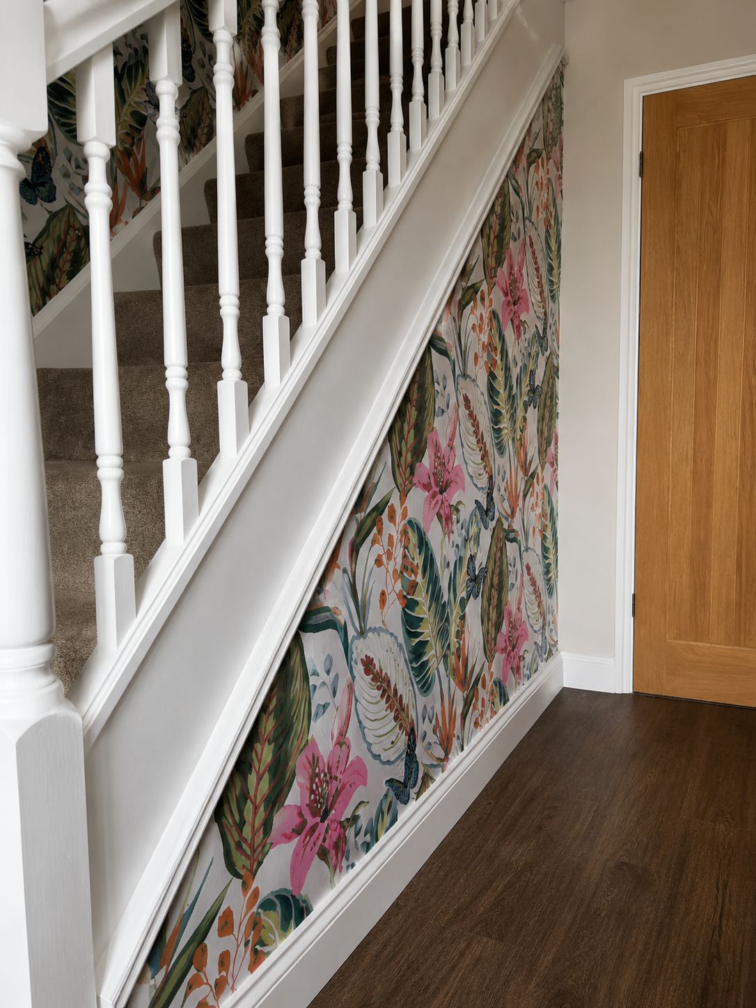 Tropical floral wallpaper running up a stairwell beside white spindles